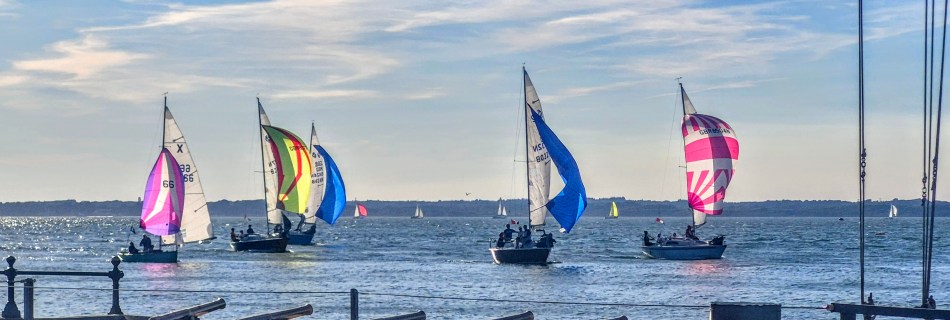 (CSF001) - Cowes Seafront - Strolling along the seafront, seeing the beautiful bright sails sailing past the Royal Yacht Squadron with the sun illuminating the brightly coloured sails.